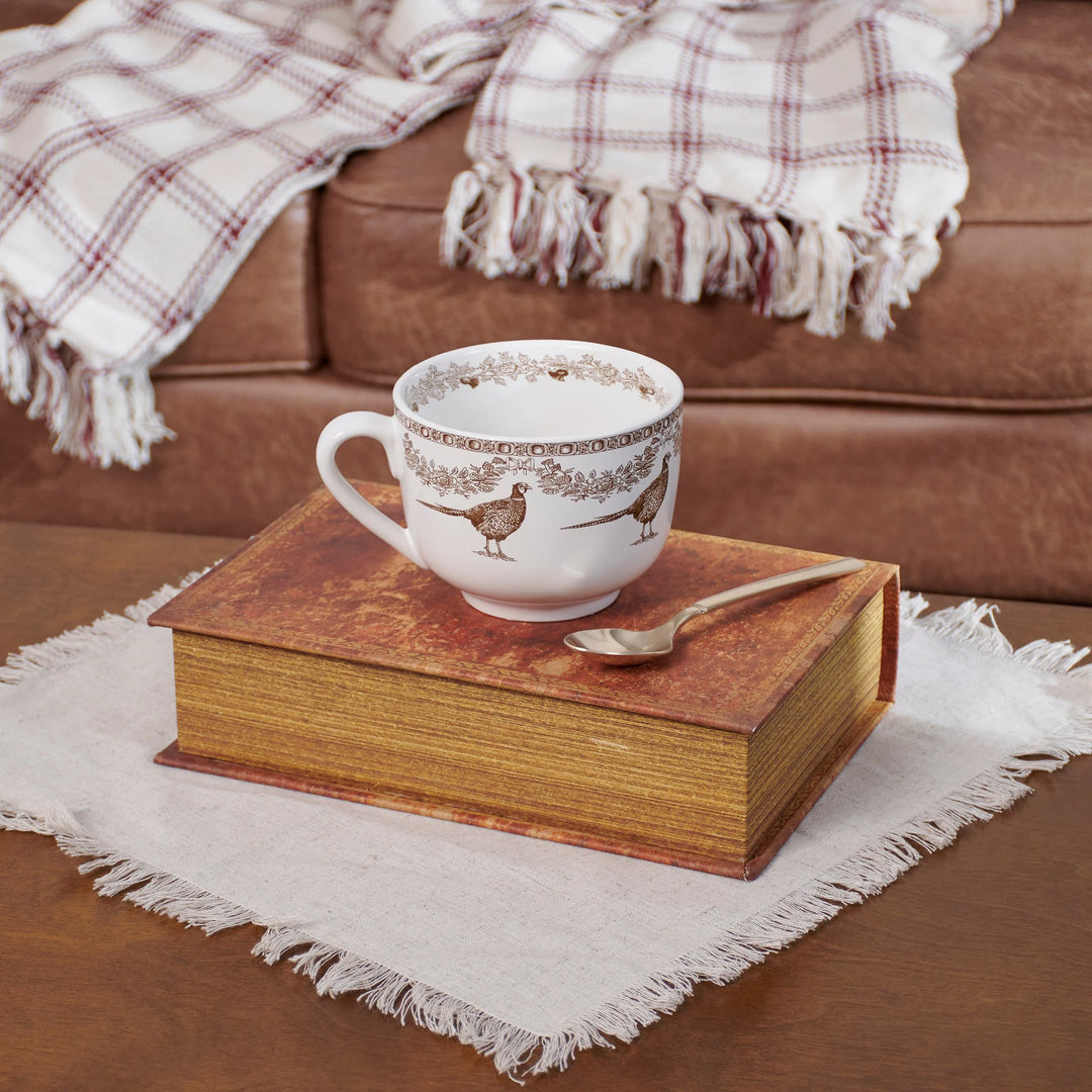 Cup with decorative design on a book on a table with a plaid blanket in the background