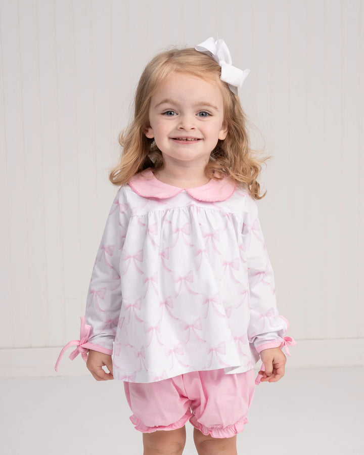 Young girl wearing a white blouse with pink collar and pink shorts on a light gray background