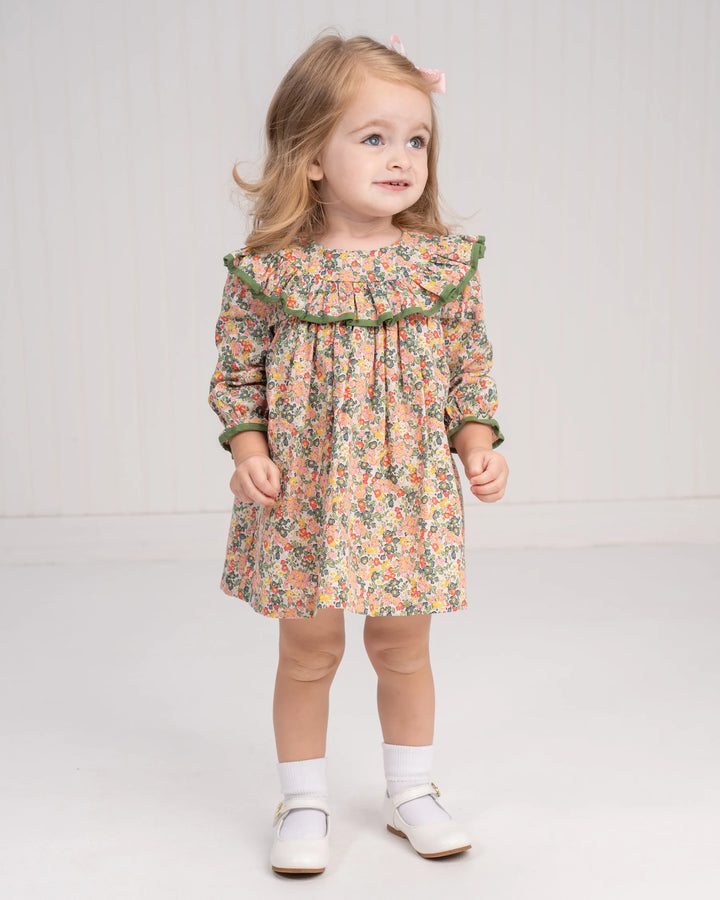 Young girl wearing a floral dress with green trim on a plain background