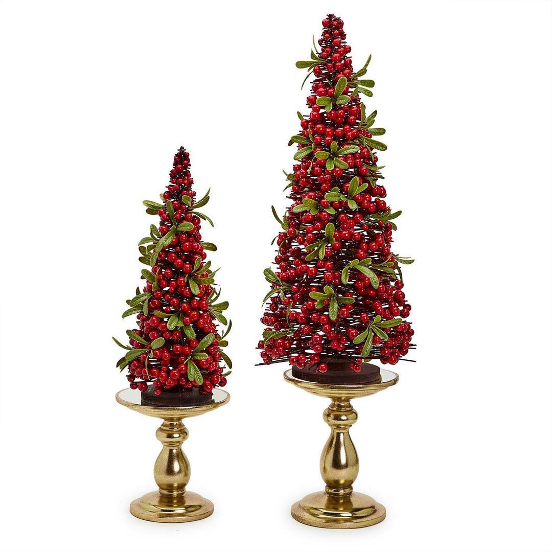 Two decorative Christmas trees with red berries on gold stands against a white background