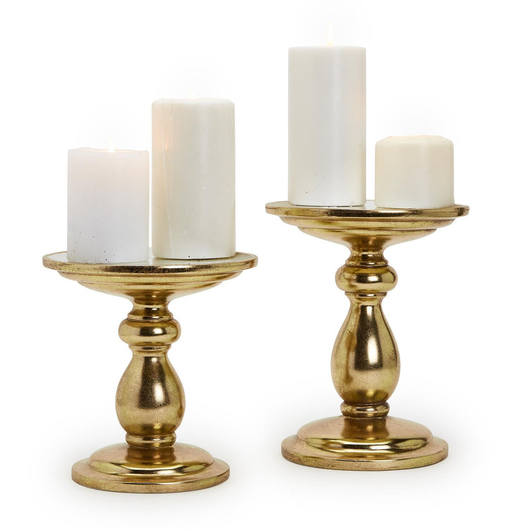 Two gold candle holders with white candles on a white background