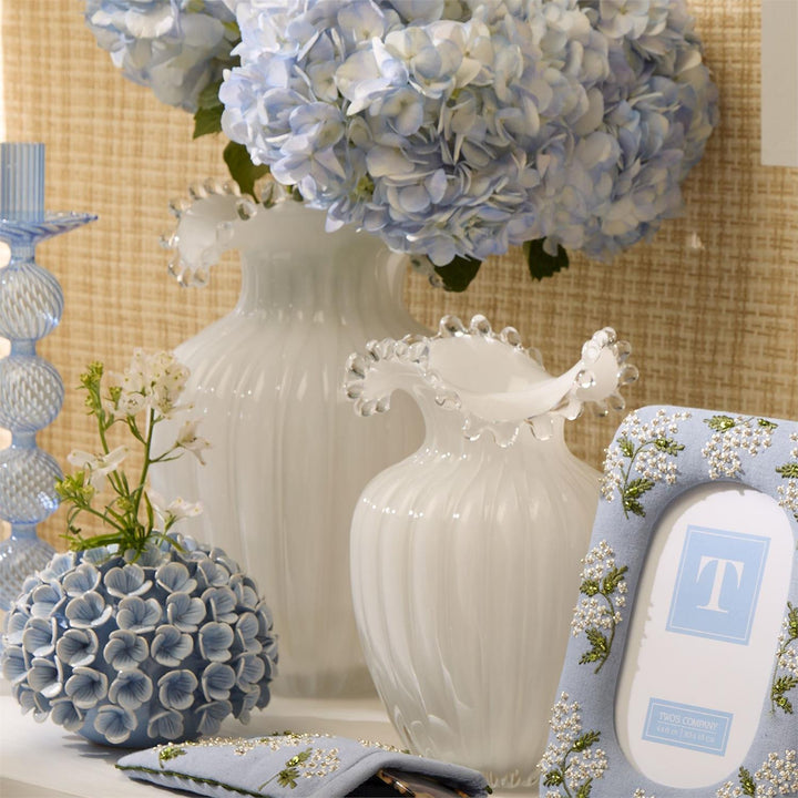 Decorative setting with white and blue vases, flowers, and a photo frame on a textured wall background.