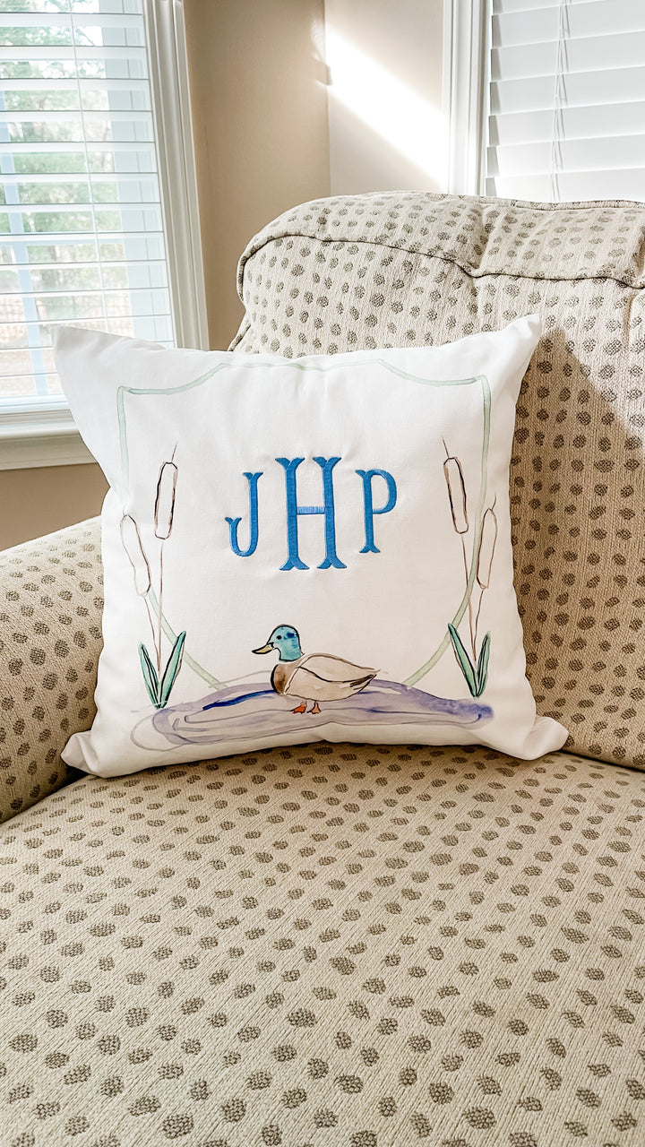 Decorative pillow with duck design and initials on a patterned couch.