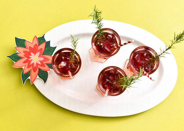 Four small glasses with red drinks and garnishes on a white plate against a yellow background