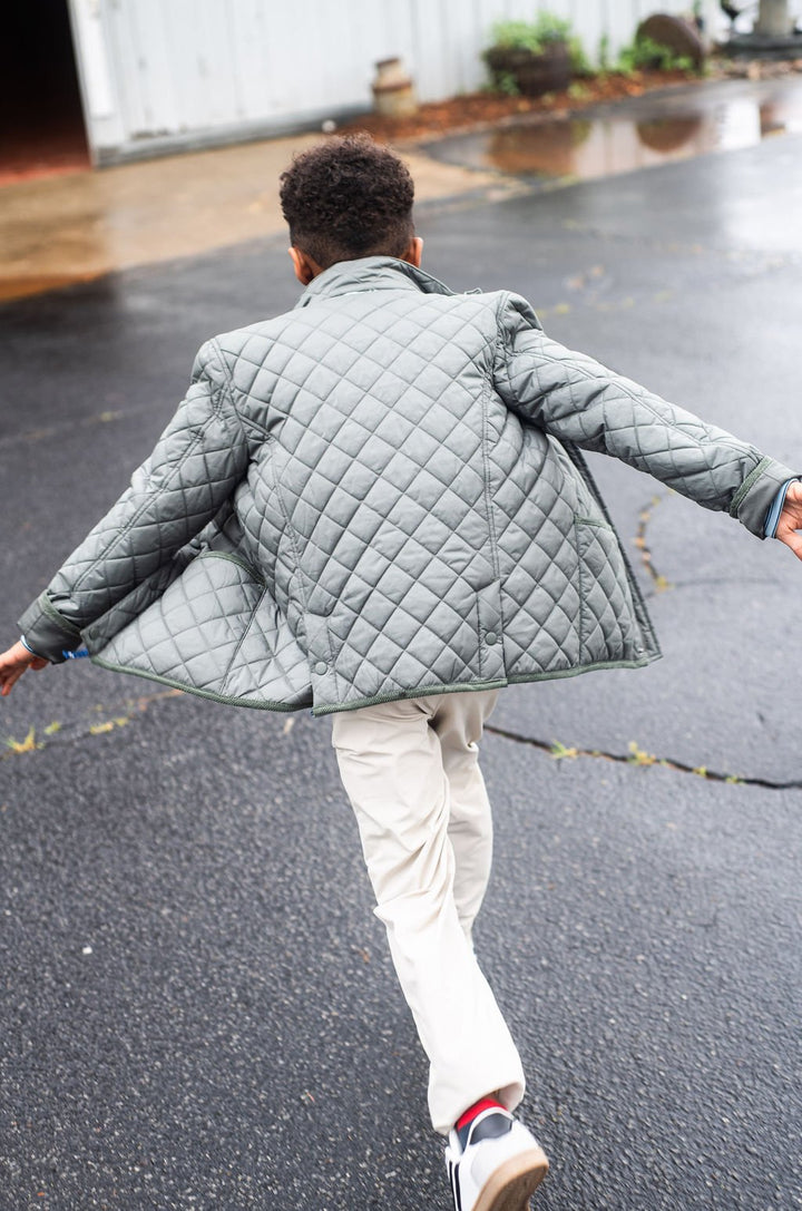Person wearing a dark green quilted jacket running on a wet pavement.