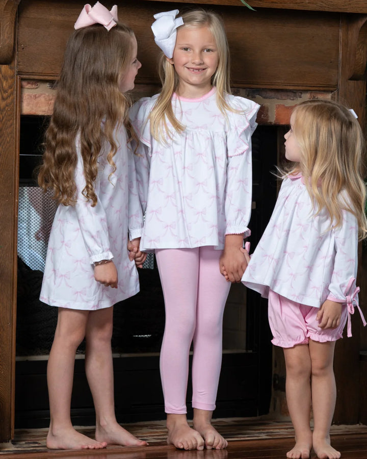 Three young girls in matching pajama sets standing in front of a wooden fireplace.
