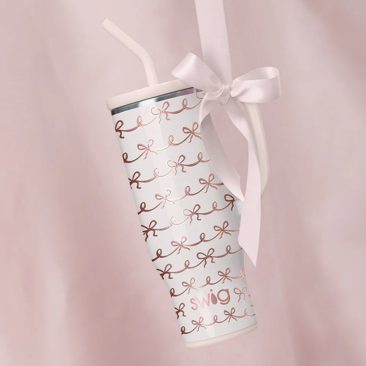 Tumbler with rose gold text and a white ribbon on a pink background