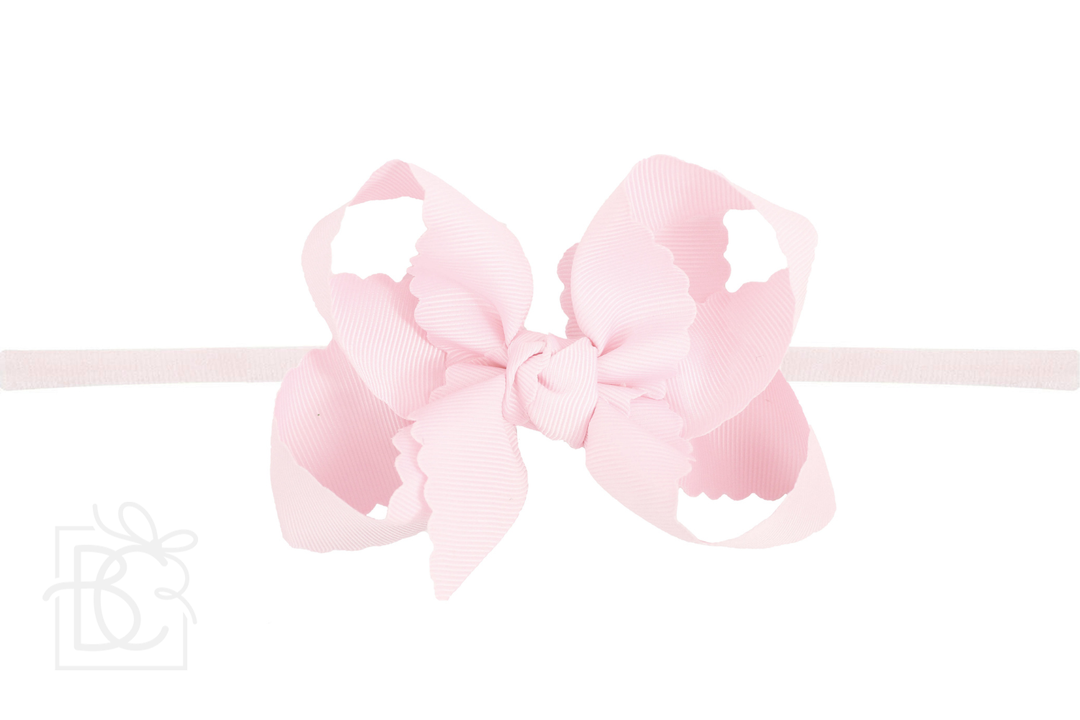 A scalloped edge bow headband in a pink color.