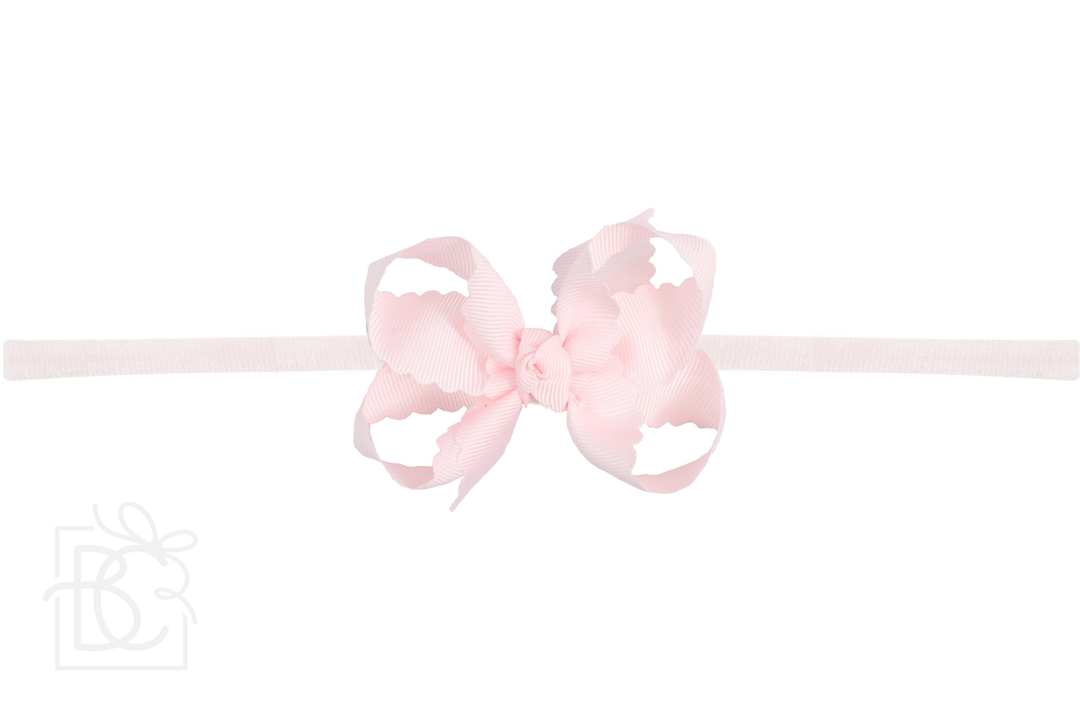 A scalloped edge bow headband in a pink color.