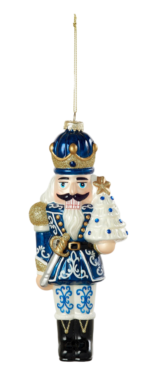 Decorative nutcracker ornament in blue and white attire with a small tree, on a white background.