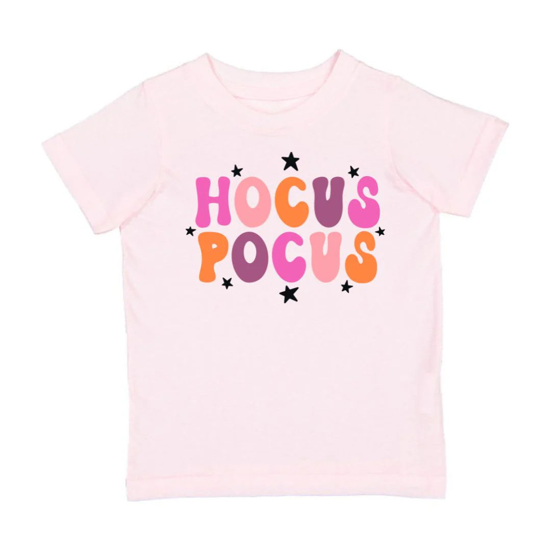Pink t-shirt with 'HOCUS POCUS' text in colorful letters on a white background