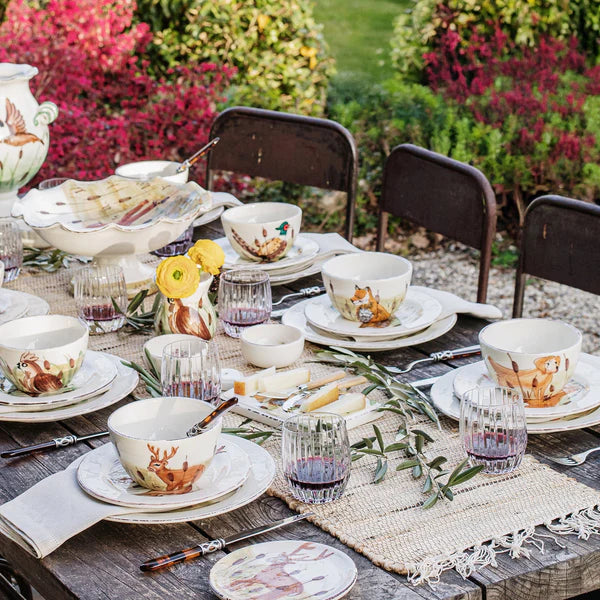 Dining table set with teacups, plates, and glasses outdoors.