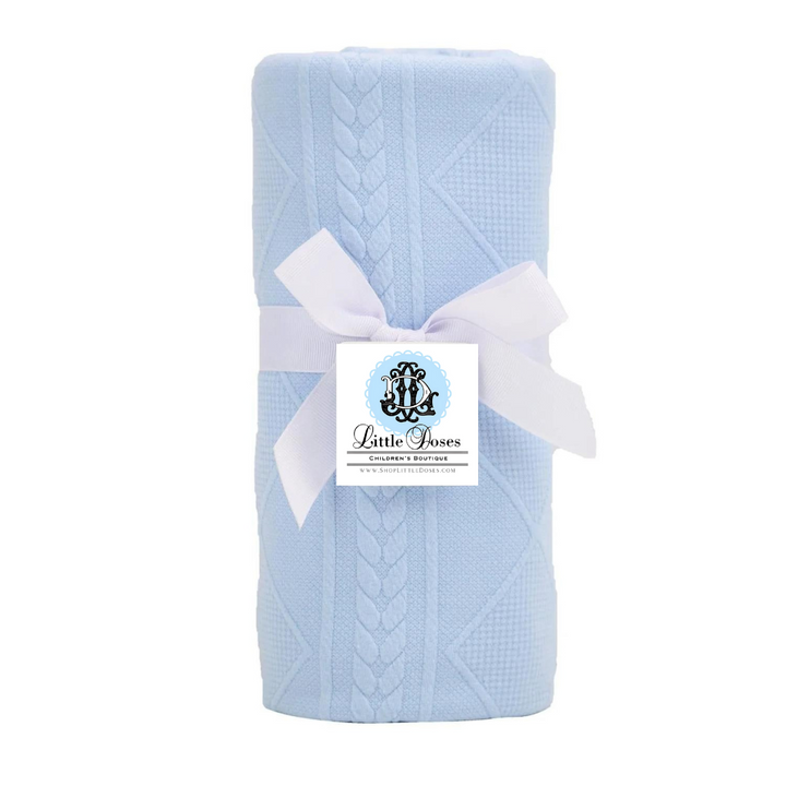 A blue knit baby blanket folded and tied with a white ribbon, displaying a tag with 'Little Foxes' branding.