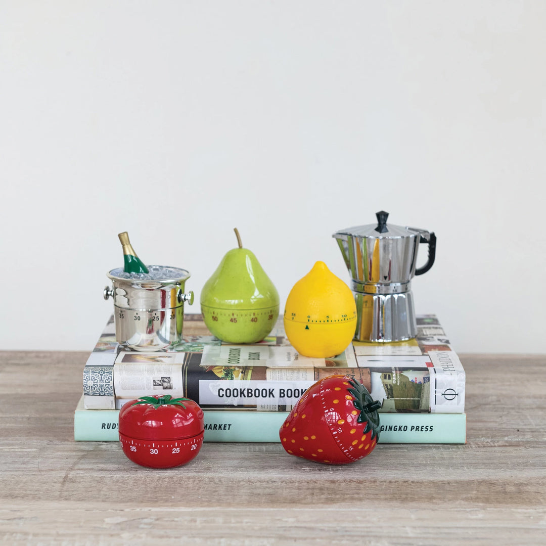 Colorful kitchen timers shaped like fruits and a coffee pot on books with a plain background