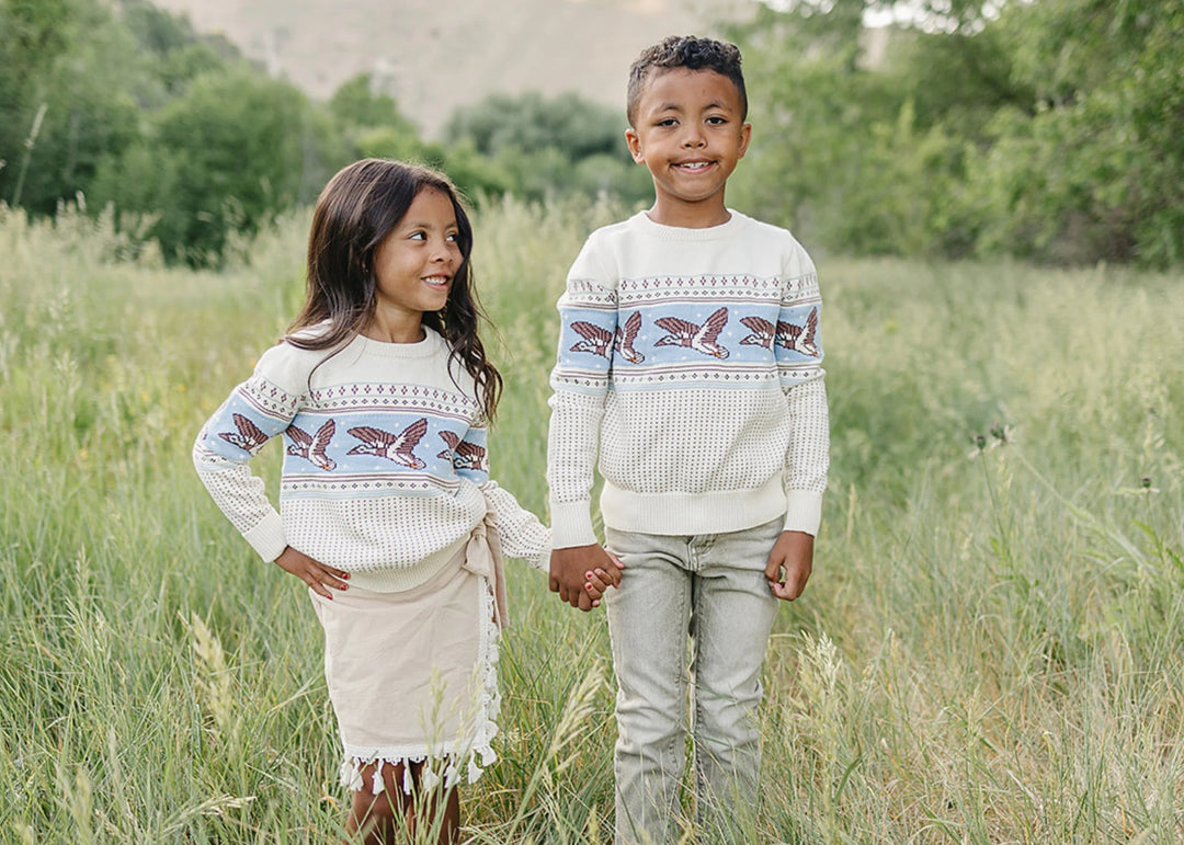 Two children wearing matching sweaters standing in a grassy field.
