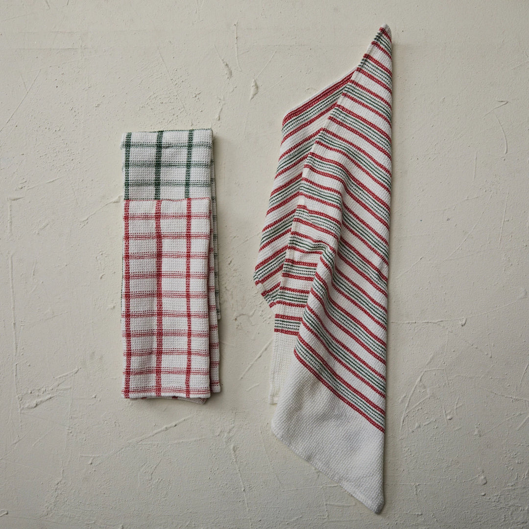 Two folded towels, one plaid and one striped, on a textured beige surface.