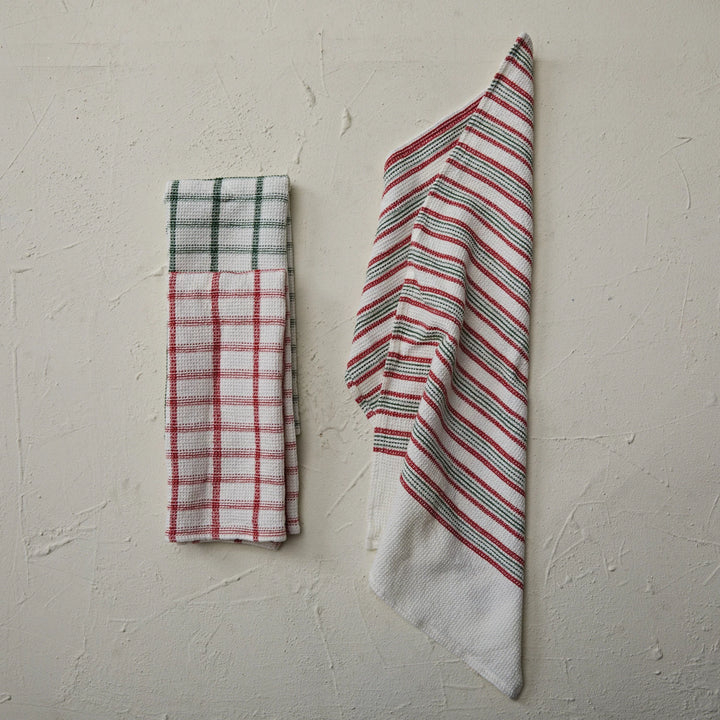 Two folded towels, one plaid and one striped, on a textured beige surface.