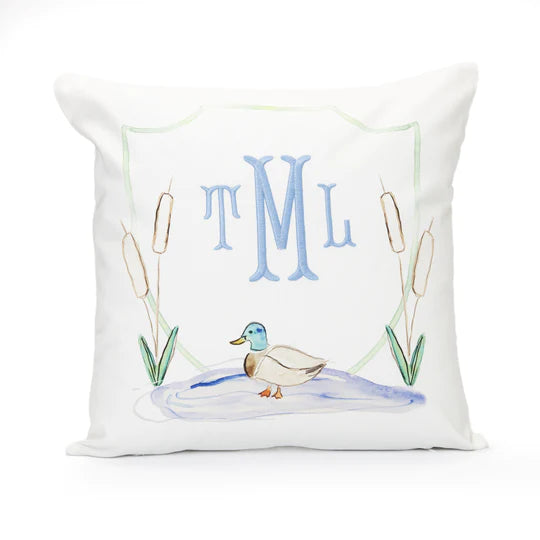 A white square pillow with a custom monogram in blue initial letters 'TML' and an illustration of a duck and reeds in blue and green.