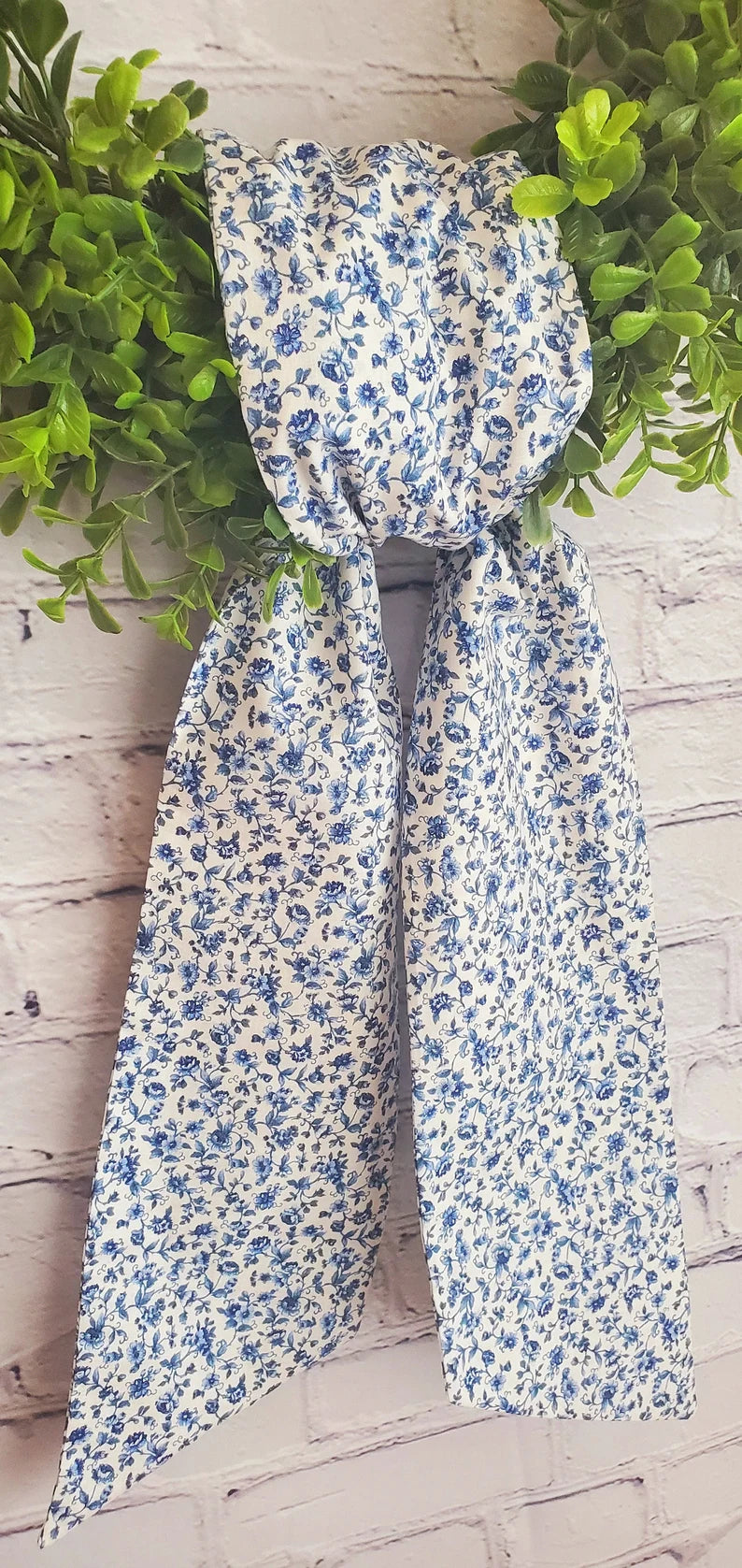 A chinoiserie inspired wreath sash with a blue and white floral pattern, displayed against a wooden background with greenery at the top.