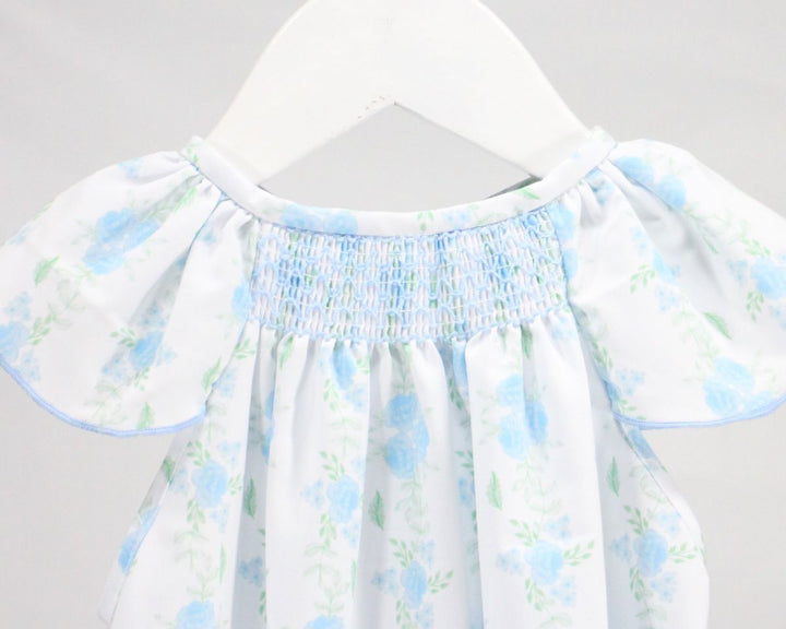 White dress with blue floral pattern on a hanger against a gray background