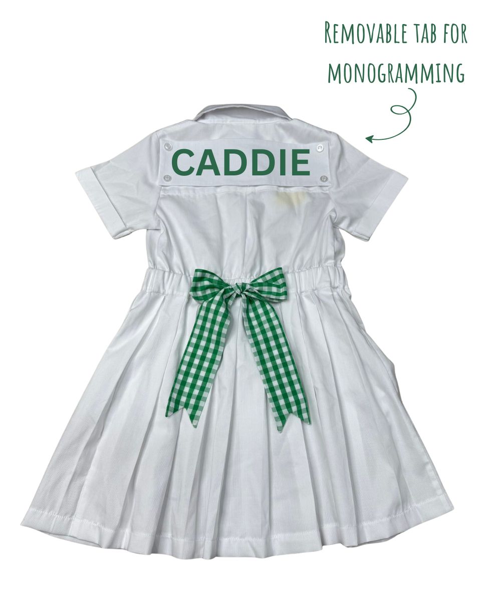 White dress with 'CADDIE' on a removable tab for monogramming, green checkered ribbon, and text indicating the feature.