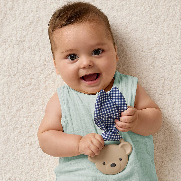 Baby holding a blue checkered bow tie against a beige background