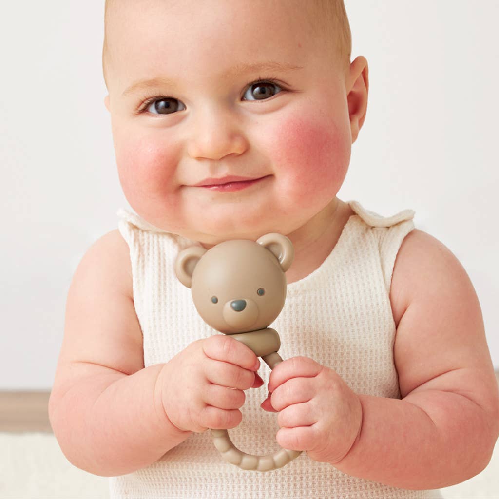 Baby holding a teddy bear-shaped rattle against a plain background