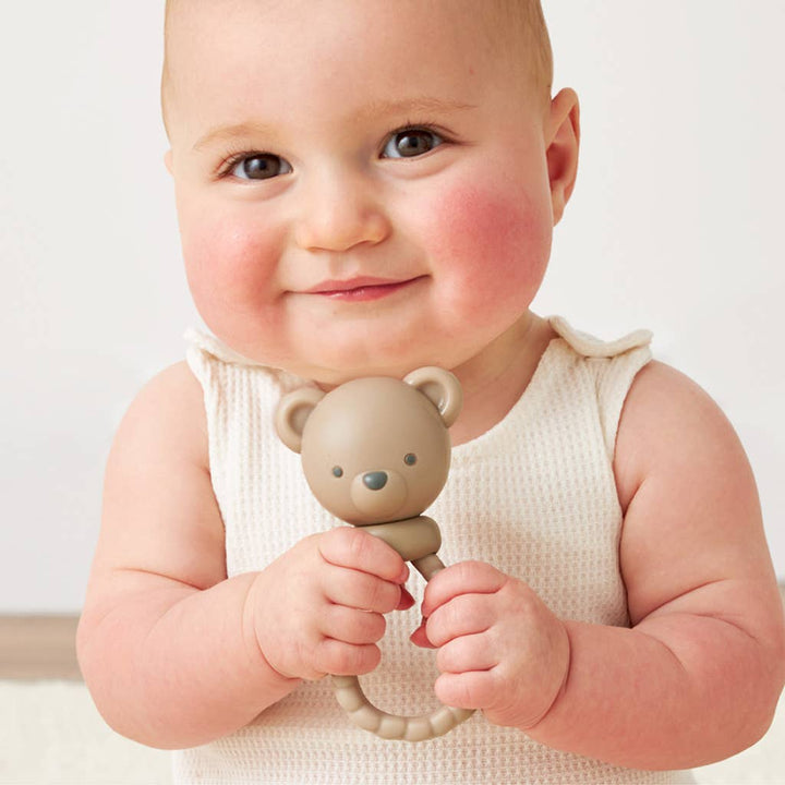 Baby holding a teddy bear-shaped rattle against a plain background