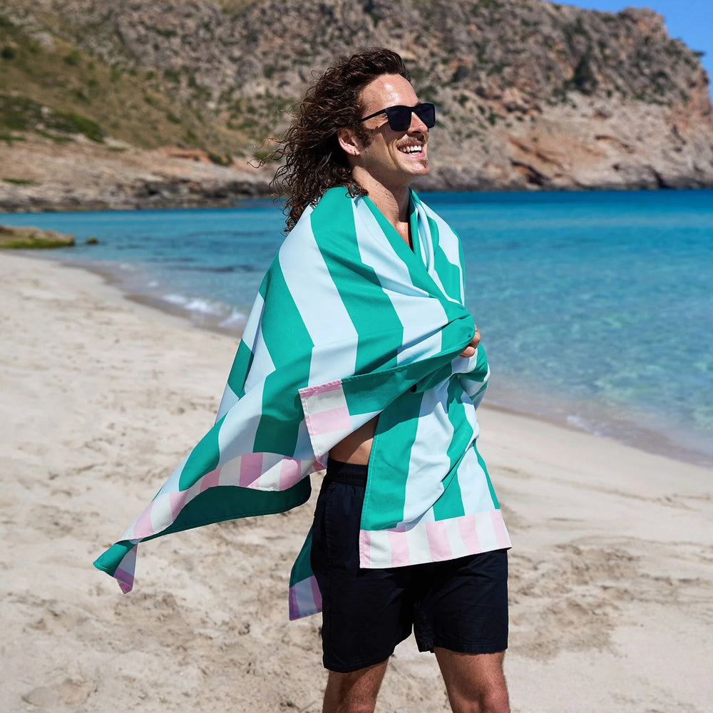 Person on a beach with a green and white striped towel draped over their shoulders.