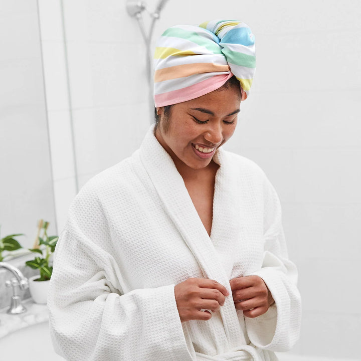 Person wearing a colorful towel on their head and a white robe in a bathroom setting.