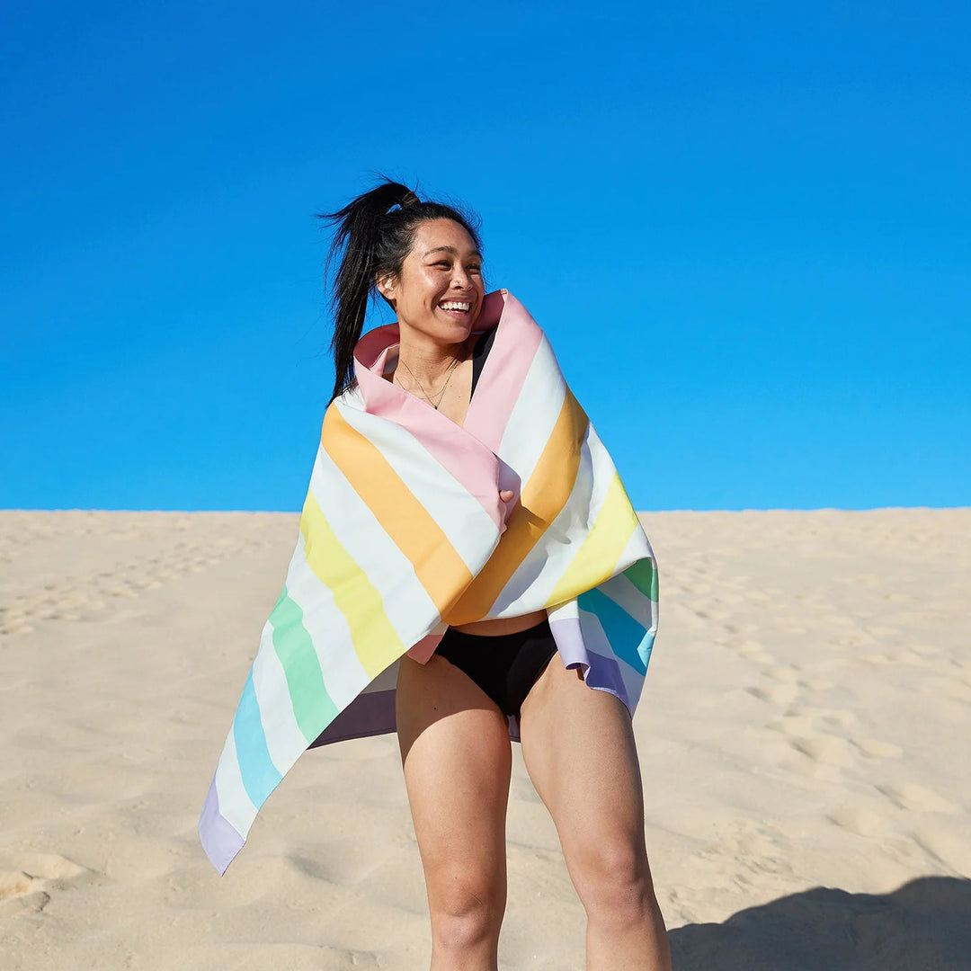 Woman wrapped in a colorful towel on a sandy beach with a clear blue sky.