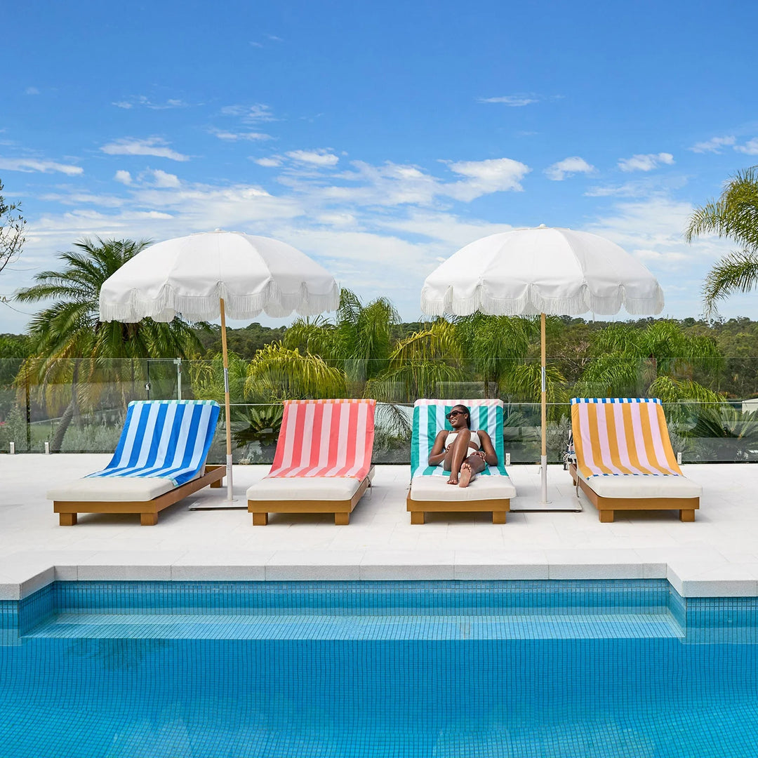 Four colorful lounge chairs with striped covers by a pool, each under a white umbrella.