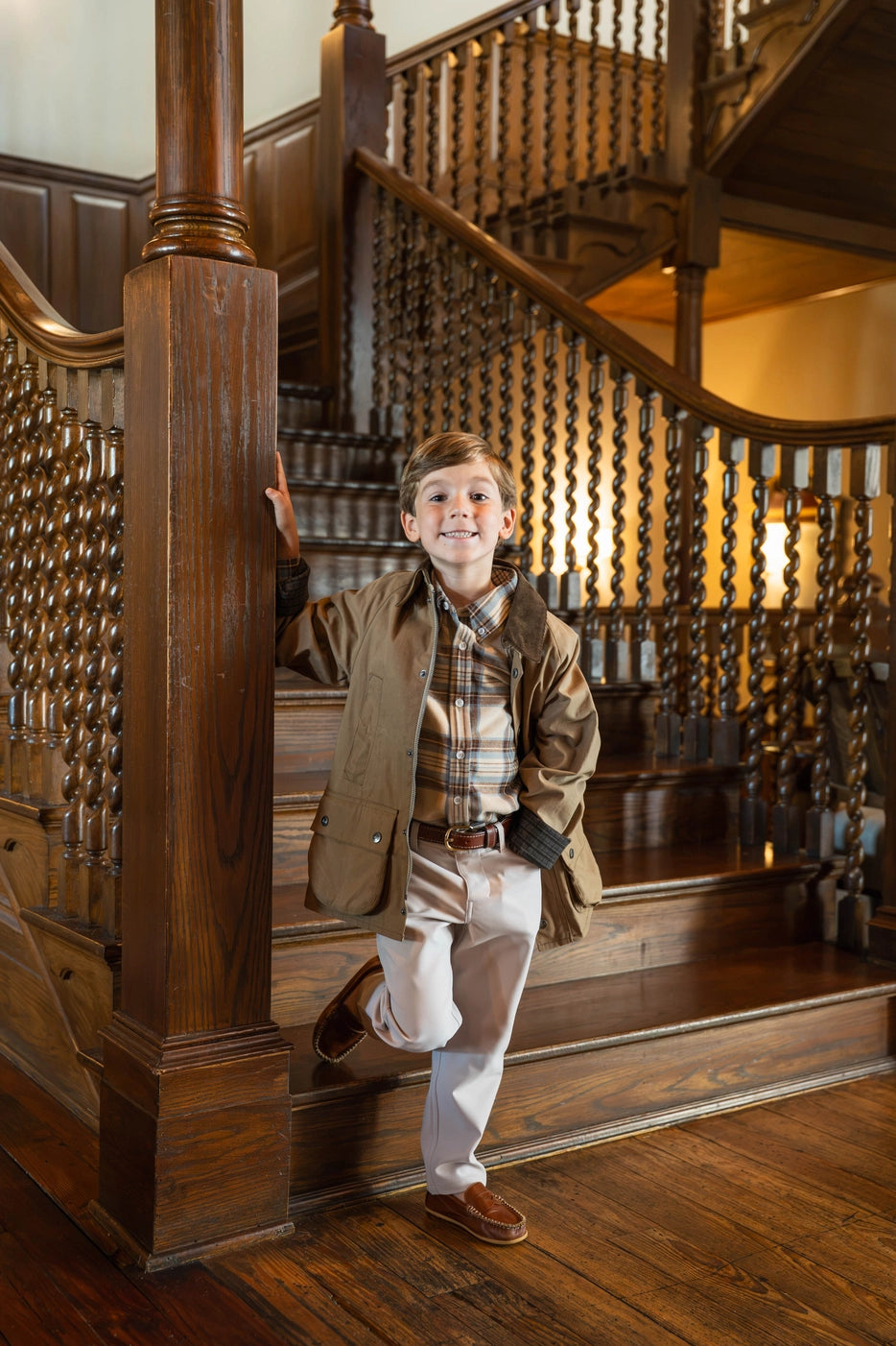 little boy wearing brown wax jacket by stairs