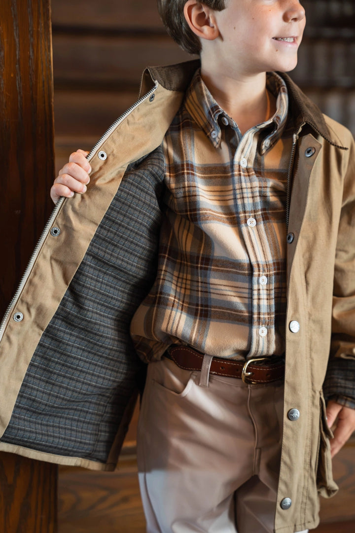 little boy wearing brown wax jacket by stairs showing inside plaid detailing