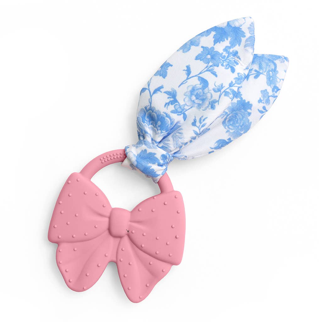 A baby teether toy featuring a textured pink silicone bow ring and a matching pink loop attached to a white fabric loop with a blue floral toile pattern, shown on a plain white background.