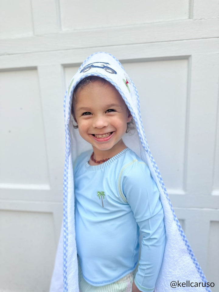 Child wearing a light blue hoodie with a hood, standing against a white wall.