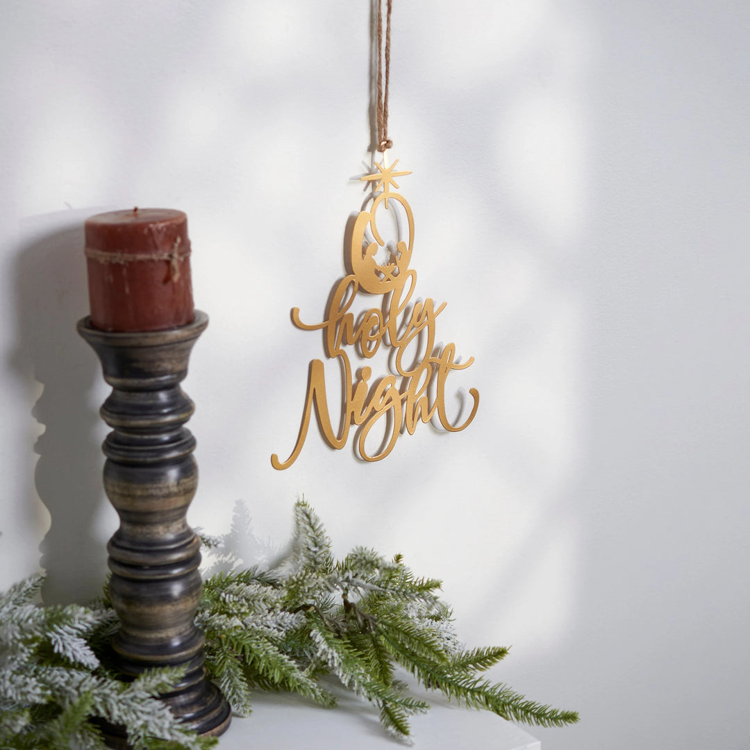 Decorative 'Holy Night' ornament hanging above a candle and greenery on a white background