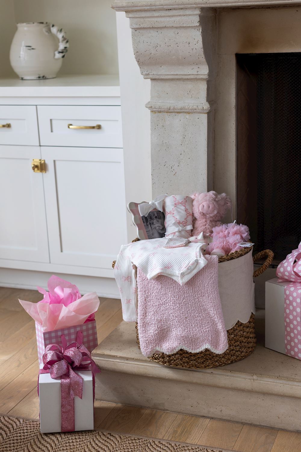 Decorative scene with pink gifts and a basket on a fireplace hearth.