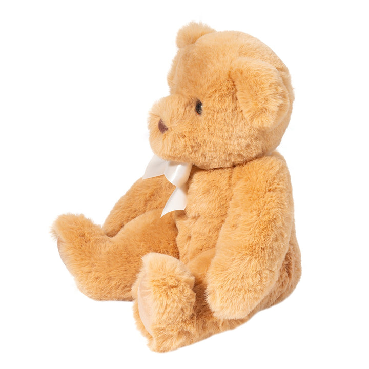 Golden brown teddy bear plush with soft fluffy fur and a cream satin bow, shown at a three-quarter angle