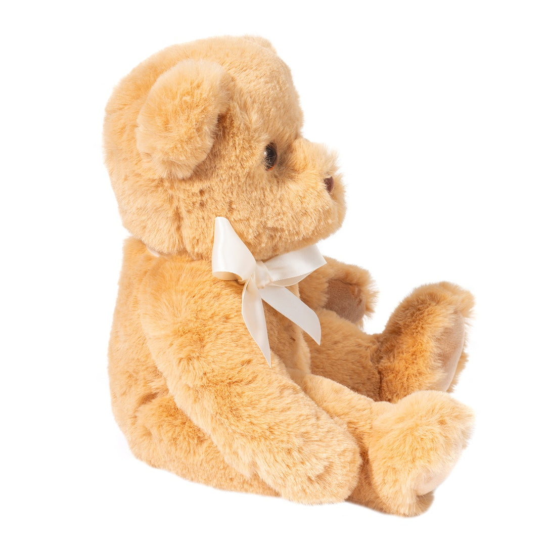 Golden brown teddy bear plush with soft fluffy fur and a cream satin bow, shown in side profile