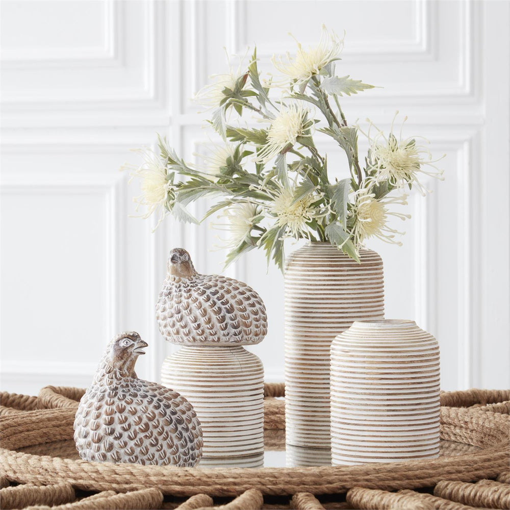 Set of decorative vases and bird figurines on a textured surface with a white paneled wall in the background.
