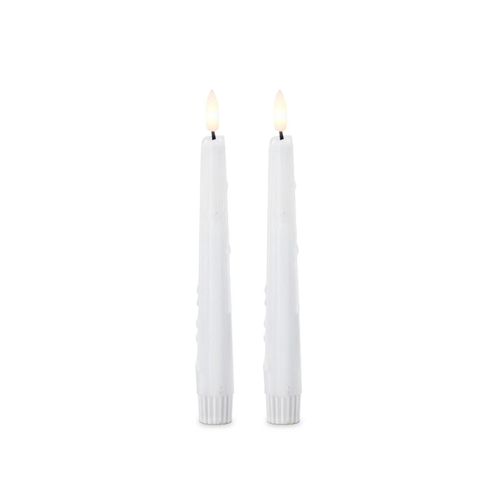 Two white candles with small flames on a white background