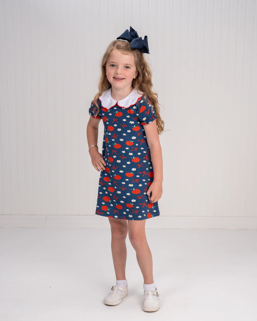 Young girl wearing a blue dress with red and white pattern on a white background
