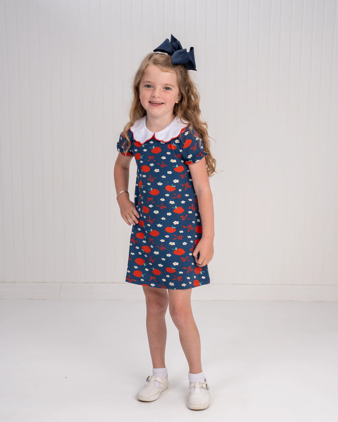 Young girl wearing a blue dress with red and white pattern on a white background