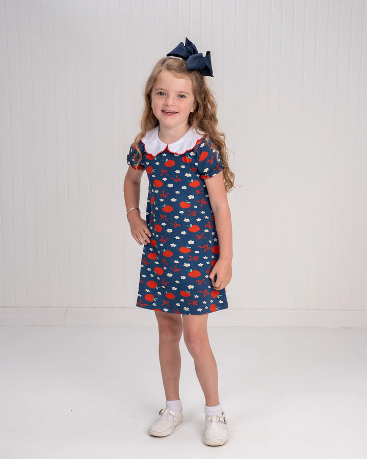 Young girl wearing a blue dress with red and white pattern on a white background