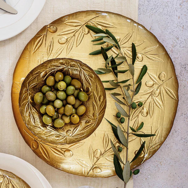 Decorative gold plate with embossed design and green olives on a neutral background