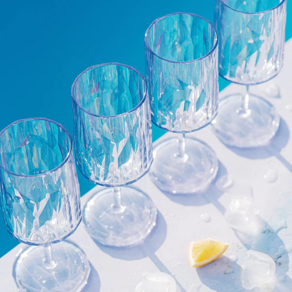 Set of four iridescent wine glasses on a blue and white checkered tablecloth with a lemon wedge.
