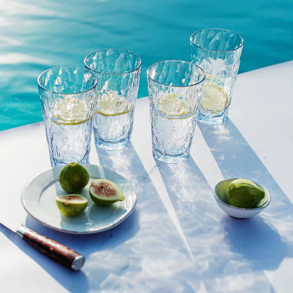 Clear glasses with lime wedges on a white surface by a pool