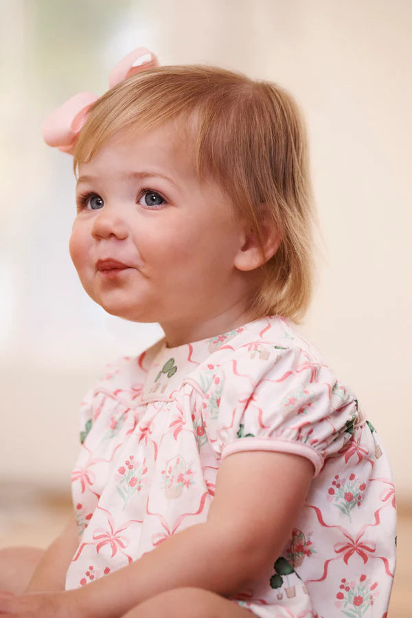 Young child wearing a floral outfit with a pink bow in their hair.