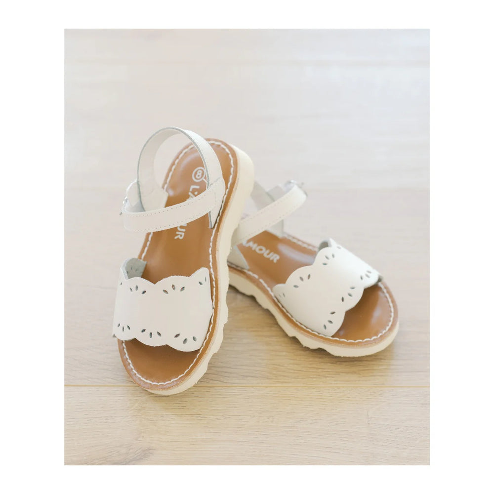 Pair of children's sandals with white straps and brown soles on a light wooden surface.